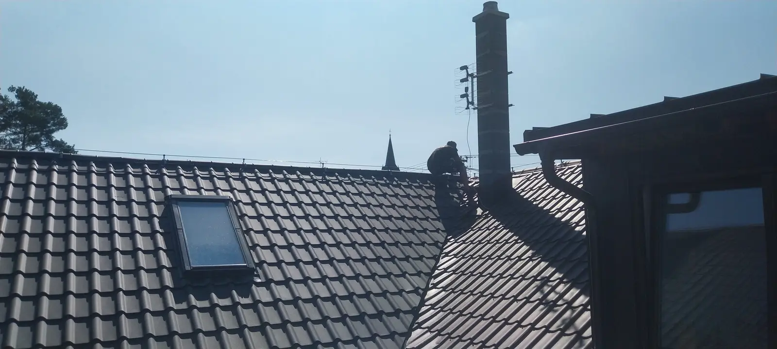 Tmavá tašková krytina se střešním oknem a komínem